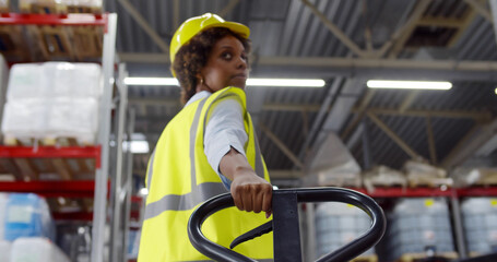 Back view of african female warehouse worker using hand pallet truck
