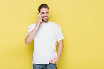 smiling man holding hand in pocket during conversation on mobile phone on yellow