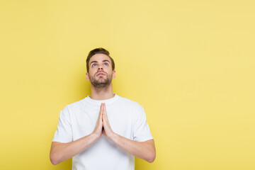 young man looking up while showing hope gesture on yellow