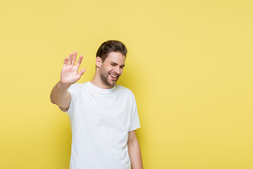 cheerful man with closed eyes showing refuse gesture on yellow