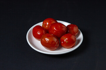 Pickled tomatoes on a black background. Pickled tomatoes on a white plate on a dark background. Canned vegetables