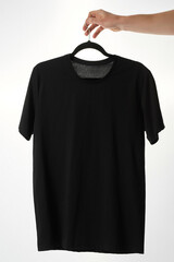 Basic wear. Hand holding black t-shirt on a hanger against white background