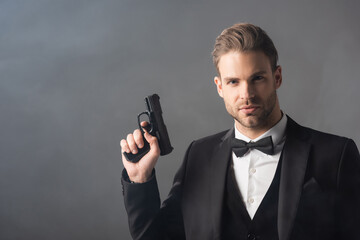 elegant businessman looking at camera while holding weapon on grey background with smoke