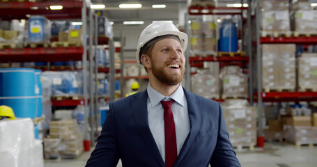 Portrait of successful young manager walking among shelves in warehouse