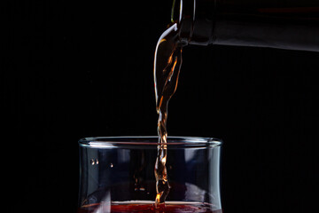 Wine is poured into a glass close-up. Wine on a black background. Red wine on a dark background. Alcoholic drink