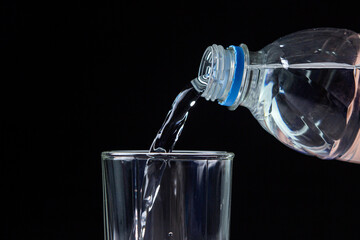 Water is poured from a bottle into a glass. Clean drinking water. Water on black background
