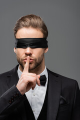 young, blindfolded businessman showing hush sign isolated on grey