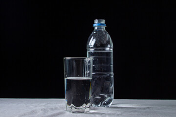Water on a black background. Pure drinking water in a bottle and in a glass. Water in a plastic bottle