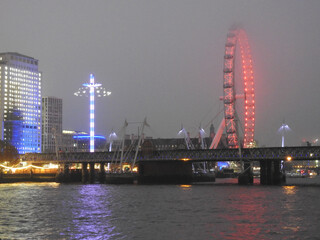 Obraz premium Illuminated observation wheel in the fog by the bridge and the river