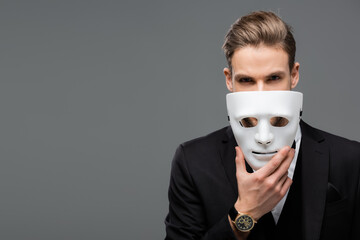 businessman holding mask near face while looking at camera isolated on grey - Powered by Adobe