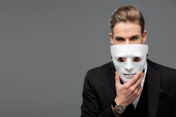 businessman holding mask near face while looking at camera isolated on grey