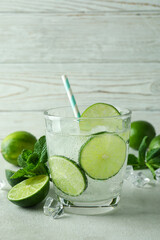 Glass of mojito cocktail and ingredients against wooden background