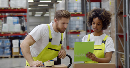 Warehouse workers sealing cardboard boxes for shipping in large warehouse