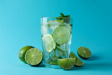 Glass of mojito cocktail and ingredients on blue background