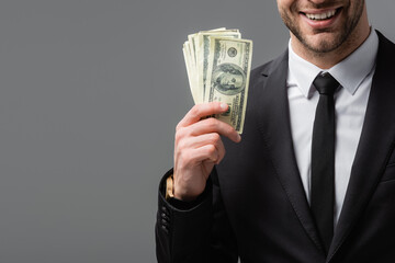 partial view of smiling businessman in black suit holding money isolated on grey