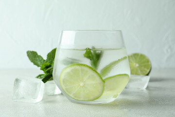 Glass of mojito cocktail and ingredients on white textured table