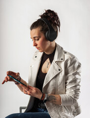 Alternative girl with tattoos using her cell phone and wireless headphones wearing a white jacket