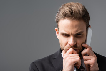 tense businessman holding hand near face while talking on mobile phone isolated on grey