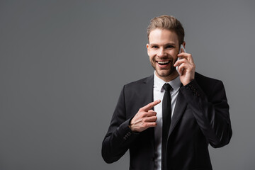 laughing businessman pointing at smartphone during conversation isolated on grey