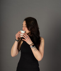 Alternative young woman with tattoos and smartwatch drinks coffee from a recyclable cup