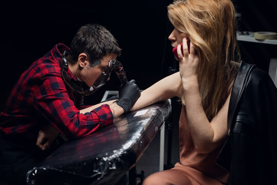 A client of a professional tattoo artist talks on the phone while making a new painless stick and poke tattoo on her arm.