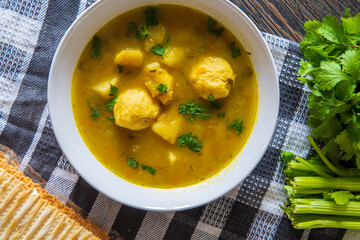 Matzo ball or kneidlach soup. Jewish traditional cuisine, homemade gluten free version. Hot and comforting matzah ball soup with vegetables. Matzos, celery and coriander in background. Top view