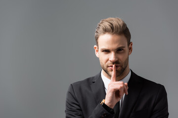 young businessman showing hush sign while looking at camera isolated on grey
