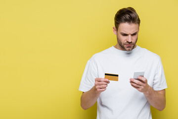 serious man typing on smartphone while holding credit card on yellow