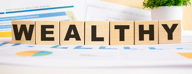 WEALTHY word on wooden cubes. The background is a business graphs. Business and finance concept