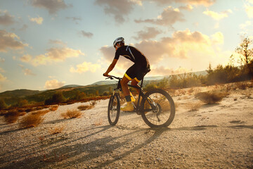 Cyclist riding a bike trough desert on  sunset. He wear full equipment for Triathlon.