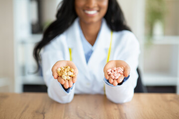 Healthy nutrition vs medication. Unrecognizable black dietitian holding tablets and nuts at table...
