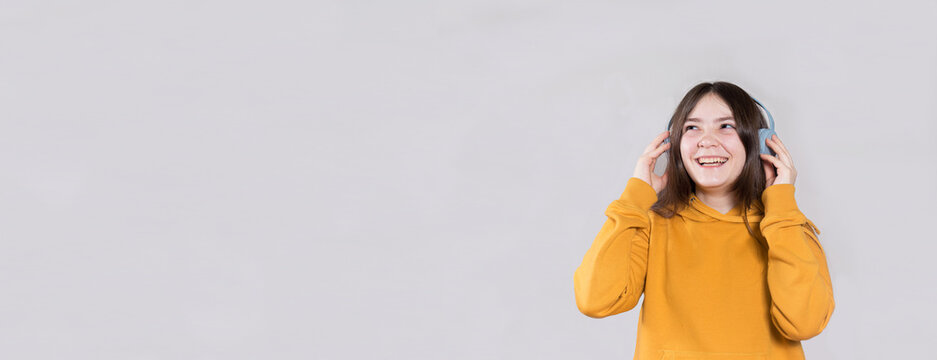 A teenage girl in a bright hooded sweatshirt on her head and headphones looks at the space for the text to the side. Learning online, schooling remotely. Banner n a light background.