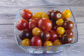 Multicolored tomatoes of different varieties in a glass bowl. Fashionable vegan food.