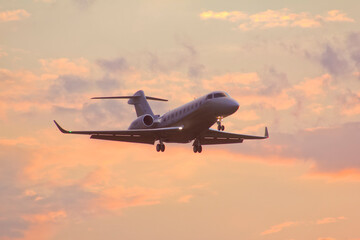 Private twin-engine jet aircraft landing at the airport with landing gear and flaps extended at sunset