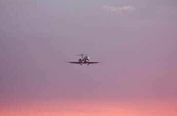 Private twin-engine jet aircraft landing at the airport with landing gear and flaps extended at sunset