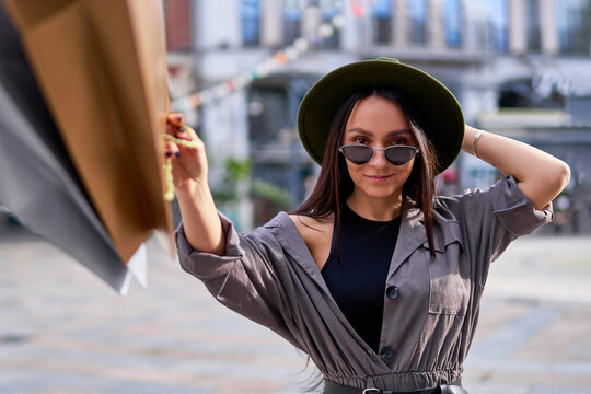 Portrait of stylish fashionable young smiling hipster woman shopaholic wearing felt hat and sunglasses with paper shopping bags during black friday sale discounts