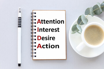 AIDA. text on white notepad paper. near cups with coffee and plants on a gray background.