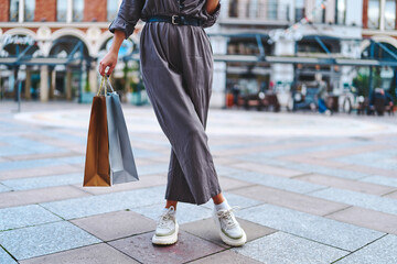Stylish fashionable woman shopaholic with paper shopping bags walks in the center of a european city during black friday sales week