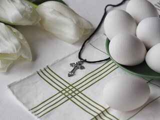 The pectoral cross lies on a white background with eggs and white tulips.Easter background concept...