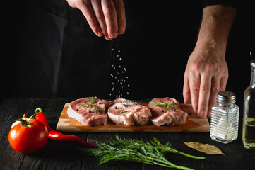 The chef sprinkles the meat with salt. Preparing meat before baking. Working environment in the kitchen of restaurant or cafe