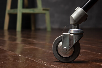 Ride on a chair leg with tangled hair on the wooden floor. Dirt stuck to the wheel. Close-up.