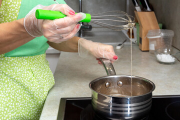 The woman raises the whisk, which drips hot sugar syrup. The cooking process. Selective focus.
