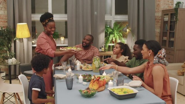 Medium PAN shot of cheerful big afro-american family having dinner together. Woman serving table while other members of family clapping hands admiring meals