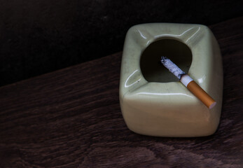 Cigarette that were burning placed on greyish green ashtray on old wooden rustic table. Copy space,...