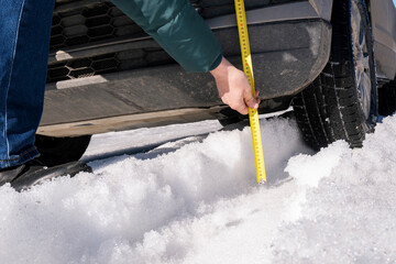 A man measures the ground clearance of a car with a tape measure . Evaluating a vehicle's off-road...