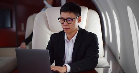 Rich asian businessman flying first class and working on plane with laptop
