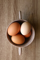 Ceramic bowl filled with fresh free range eggs on wooden table. Flat lay.