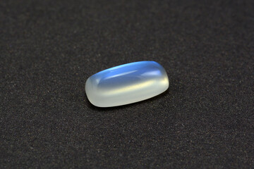 Natural genuine adularia blue sheen barrel cabochon moonstone. Loose clean crystal gem on gray textured leather background. Feldspar mineral group. Semiprecious gemstone for jewelry making. 