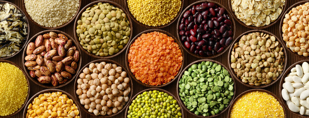 Various colorful legumes and cereals in bowls background.