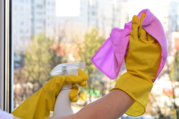 women's hands in yellow household gloves clean the window with a pink napkin. Cleaning concept.